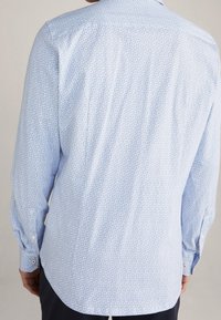 Jasnoniebieska koszula z długim rękawem, wykonana z miękkiej tkaniny z delikatnym wzorem na całej powierzchni, z klasycznym kołnierzykiem i zapinanymi mankietami.