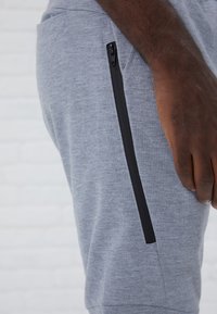Gray joggers feature a side zip pocket with black hardware. Fabric has a soft texture, and the design includes a tapered fit.
