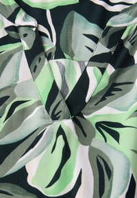 Kwiatowa bluzka z dekoltem w kształcie litery V, w odcieniach zieleni i czerni, z dużymi abstrakcyjnymi wzorami liści oraz miękkim, teksturowanym materiałem.