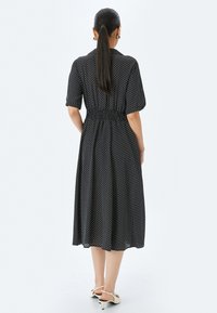 Mustassa pilkullinen mekko, jossa on lyhyet puffihihat, smokkikuvioitu vyötärö ja midi-pituus, valmistettu kevyestä kankaasta; yhdistetty valkoisiin korkokenkiin.