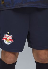 Marinblå fotbollsshorts i strukturerad stomme med Red Bull Salzburg-logotyp som visar röda tjurar, fotboll och en stjärna ovanför.