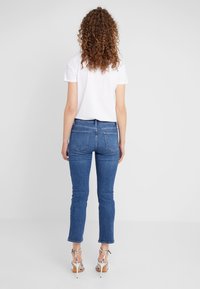 Jeans de denim de corte ajustado en azul medio, con una cintura de altura media, cinco bolsillos y un ligero efecto de desgaste. Combinados con una camiseta blanca básica.