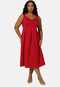 Punainen A-linjainen mekko V-muotoisella kaula-aukolla, laskostetulla hameella ja säädettävillä olkaimilla. Pehmeä kangas, joka on lentävän tuntuinen, nilkkapituinen.