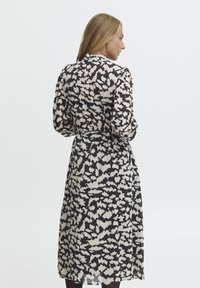 Abito lungo con un motivo astratto bianco e nero, in tessuto leggero, colletto e vita svasata, con maniche lunghe e una silhouette fluida.