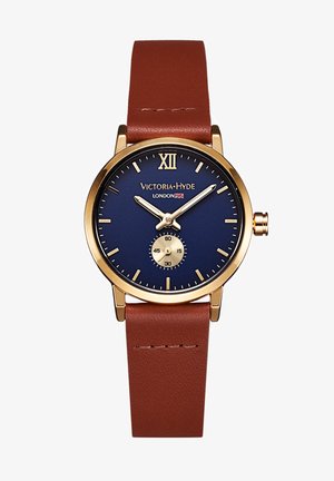 Montre avec bracelet en cuir marron, boîtier doré, cadran bleu, index horaires dorés et un petit sous-cadran en bas pour les secondes. Le chiffre romain XII est positionné en haut.