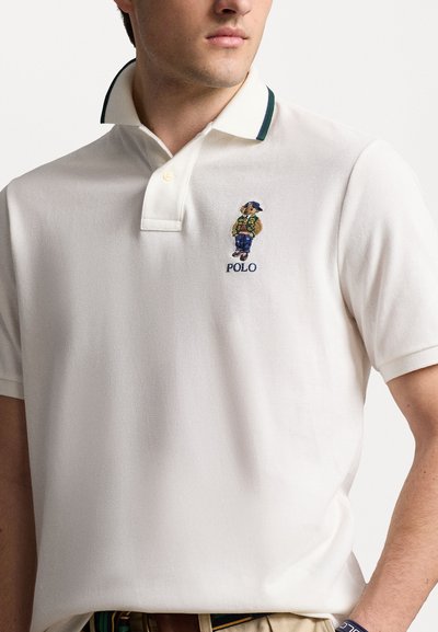 Polo blanc en tissu texturé. Il présente un col en côtes contrasté et un logo d'ours brodé. Col boutonné et coupe décontractée.