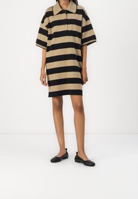 Randig polo-klänning i beige och svart, korta ärmar, knäppt krage, avslappnad passform, slät textur, kombinerad med svarta ballerinas.