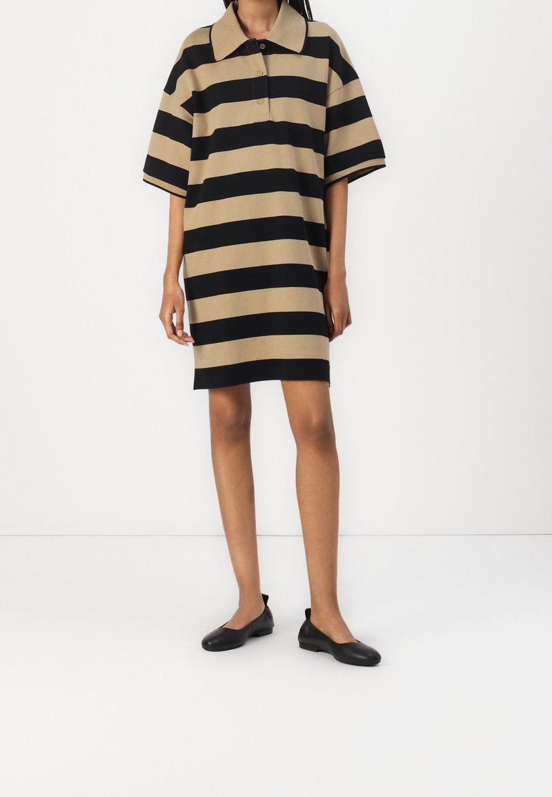 Randig polo-klänning i beige och svart, korta ärmar, knäppt krage, avslappnad passform, slät textur, kombinerad med svarta ballerinas.