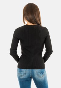 Maglione nero a coste con maniche lunghe, scollatura rotonda e silhouette aderente, abbinato a jeans blu con tasche decorative sul retro.