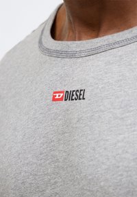Γκρι βαμβακερό T-shirt με στρογγυλή λαιμόκοψη, με μικρό κόκκινο και μαύρο λογότυπο "DIESEL" στο στήθος. Υφή ύφανσης με εμφανείς ραφές.