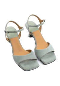 Grüne Wildleder-Sandaletten mit Rechteckzehe, Knöchelriemen und hellbraunem Fußbett. Sie verfügen über einen niedrigen Blockabsatz.