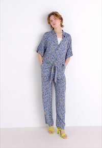 Sinine lillemustriga jumpsuit lühikeste varrukatega, mugav lõige ja lipsuga vöö. Koos kollaste kõrgete kontsadega sandaalidega.