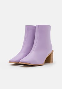 Fialové kotníkové boty vyrobené z hladké kůže, s špičatou špičkou a dřevěným patníkem, s elegantním a bezproblémovým designem.