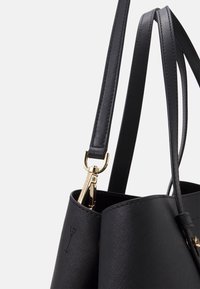 Musta teksturoitu nahkakäsilaukku kultaisilla yksityiskohdilla, jossa on kaksi ohutta hihnaa ja tyylikäs solkiyksityiskohta sivussa.