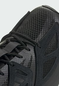 Scarpe sportive nere con tomaia in rete, sovrapposizioni sintetiche testurizzate, lacci piatti e una suola robusta con motivi di presa pronunciati.