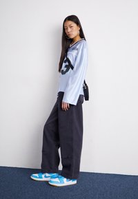 Chemise à manches longues bleu clair avec des accents noirs et le numéro 23, associée à un pantalon large noir et des baskets bleu et blanc.