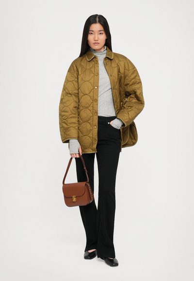 Piekļautā olīvu zaļā jakā, pelēkā tārte, melnajās platās biksēs, brūnā plecu somā ar zelta detaļām un melnā apavos.