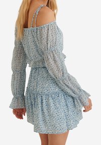 Lyseblå blomsterkjole med lange, puffede ærmer og off-shoulder design, med flæset kant og indsnævret talje for tekstur og form.