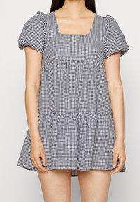 Zwart-witte ruitjesjurk met een vierkante halslijn, pofmouwen en een gelaagde rok. Gemaakt van lichtgewicht stof, met een comfortabele pasvorm.