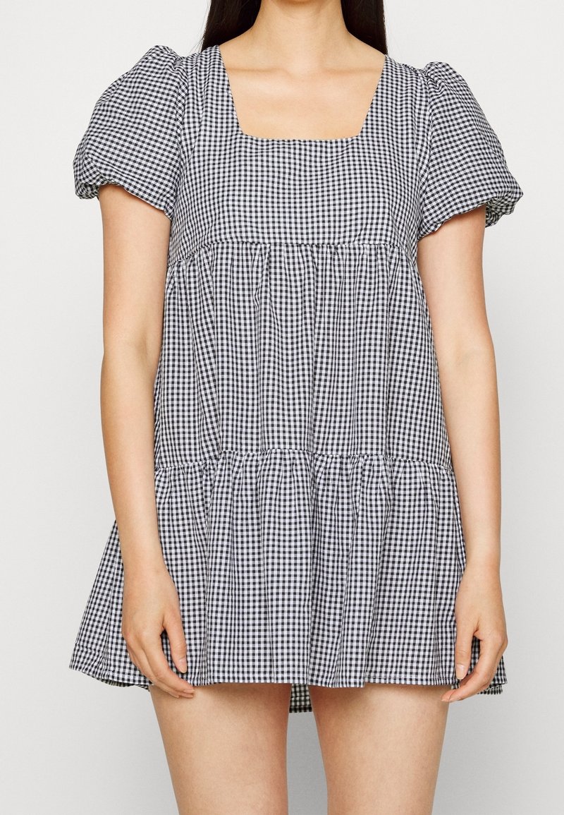 Zwart-witte ruitjesjurk met een vierkante halslijn, pofmouwen en een gelaagde rok. Gemaakt van lichtgewicht stof, met een comfortabele pasvorm.