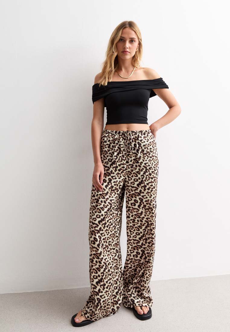 Schwarzes, schulterfreies Crop-Top, kombiniert mit beigen, weit geschnittenen Hosen mit braunem Leopardenmuster und einem elastischen Bund.