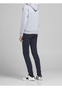 Šedá mikina s kapucí a přední kapsou, námořnické slim-fit kalhoty a bílé tenisky s modro-červenými akcenty na patě. Hladké textury látek.