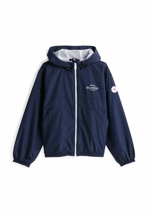 Chaqueta cortaviento de color navy con un zipper blanco, capucha forrada de malla, puños elásticos y un logotipo bordado prominente en el pecho y la manga.