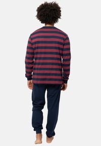 Top a maniche lunghe, a righe blu navy e bordeaux, abbinato a pantaloni blu navy. Il tessuto sembra morbido, con una vestibilità casual e polsini a coste.