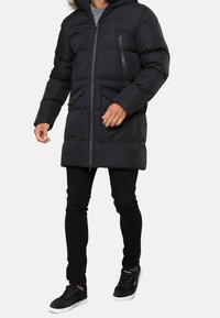 Sort dynejakke med hætte, der har lynlåslommer på brystet og sidelommer med lapper. Glat tekstur, lange ærmer og knælængde.