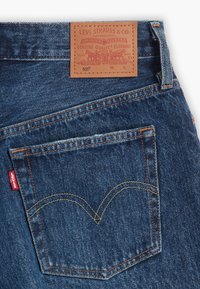 Poche arrière du jean Levi's 501 bleu avec coutures jaunes, étiquette rouge Levi's et étiquette en cuir beige Levi Strauss & Co. sur la ceinture.