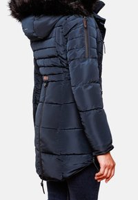 Mörkblå vadderad jacka med luva kantad med päls, vertikal sömnad, fickor med dragkedja och en lätt rundad nederkant. Vattentätt material.