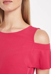 Top mit kaltem Schulterdesign aus leuchtend pinkem Stoff. Mit Rüschensleeves und glatter Textur. Sauberer Ausschnitt und dezente Seitentaschen.