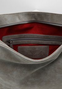 Grijze leren tas interieur met een rode voering, voorzien van een ritssluiting zak en een label met een reliëf van een hart en vleugels ontwerp.