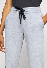 Pantalones joggers de algodón gris con cintura elástica, cordón negro, bolsillos laterales y textura sutil. Marca visible cerca del dobladillo.