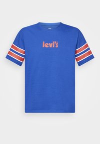 Camiseta de algodón azul con mangas cortas. Acentos de rayas rojas y blancas en las mangas. Presenta el logo de "levi's" en naranja en el pecho.