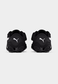 Μαύρα αθλητικά παπούτσια Puma με λευκό λογότυπο στη φτέρνα, εμφανιζόμενα από πίσω, με υφασμένα πέλματα και μαύρο μαξιλάρι γύρω από τον αστράγαλο.
