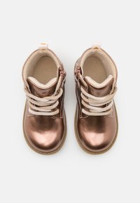 Un par de botas para toddler en un brillante color oro rosado, con cordones beige, forro de felpa suave y cremallera lateral, vistas desde arriba sobre un fondo blanco.