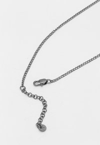 Zilveren metalen ketting met een kleine sluiting, voorzien van links van gelijke grootte en een ronde label nabij de sluiting.