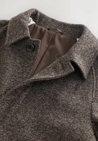 Pruun herringbone-stiilis villane mantel pöördkaelusega, mustade nuppudega ja sujuva sobiva pruuni voodriga, mis on seest nähtav.