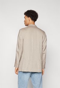 Beige blazer with a textured finish, single back vent, and buttoned cuffs, paired with light blue jeans.