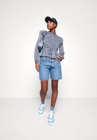 Top a quadri con maniche arricciate, vita cinchata, e pantaloni corti di denim blu. Sneakers blu e un cappellino navy completano l'outfit informale.