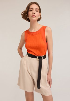 Orange ribbed tank top with a sheer neckline, paired with beige pleated shorts and a black belt featuring a gold circular buckle.