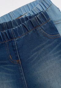 Due paia di jeans in varie tonalità di denim blu. Entrambi presentano cinturini elasticizzati e dettagli di cucitura visibili.