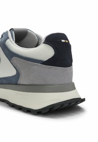 Talon de basket avec panneaux en mesh gris, marine et blanc, surpiqûres en daim, semelle en caoutchouc noir, et "BOSS" embossé sur la semelle intermédiaire blanche.