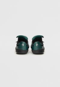 Zapatillas verdes y negras con una parte superior lisa y texturizada, un cuello acolchado y detalle de logo en el talón. Suela de goma.