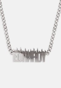 Collana in metallo argentato con il nome "ED HARDY" caratterizzata da un design a bordo frastagliato, collegata da una catena spessa.