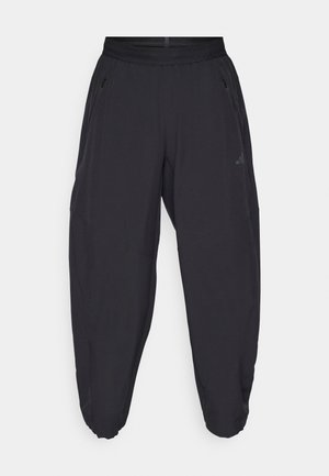 Black athletic pants with elastic waistband, zippered side pockets, tapered legs, and subtle logo on the right thigh.