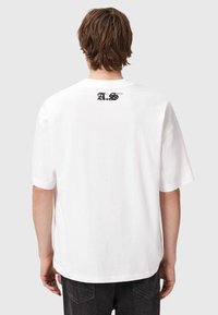 Valge puuvillane T-särk, mis on ümara kaelusega ja lühikeste varrukatega, musta "A.S." logoga selja ülaservas.