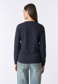 Maglione blu navy con scollatura rotonda, maniche lunghe e orlo a costine. Il tessuto sembra morbido e texturizzato, abbinato a jeans in denim azzurro chiaro.