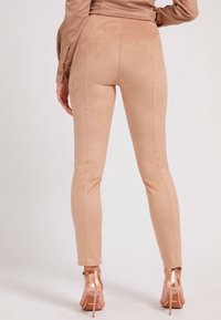 Leggings beige in finta pelle scamosciata, dalla vestibilità slim e con cuciture laterali, abbinati a sandali con tacco alto lucidi color oro rosa.
